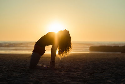 Woman exercising on beach during sunset