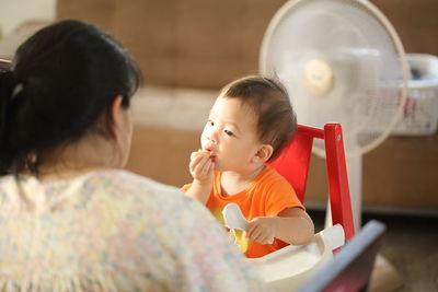 Rear view of mother against baby boy sitting on high chair at home