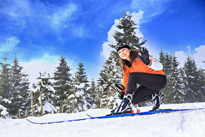 Portrait of woman wearing ski sitting on snow covered field 