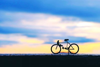 Bicycle by sea against sky during sunset