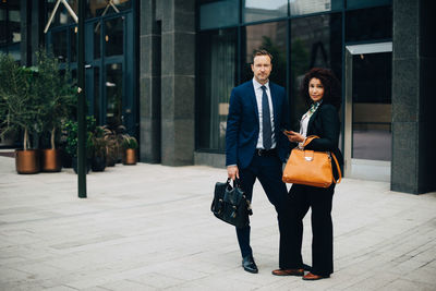 Full length portrait of confident businessman and businesswoman standing against building in city