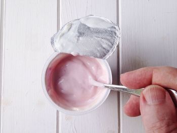 Cropped hand eating yogurt on white table