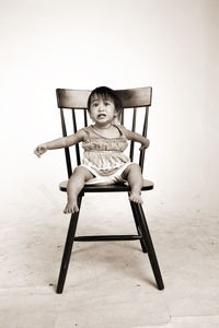 Baby girl looking away while sitting on chair against white background