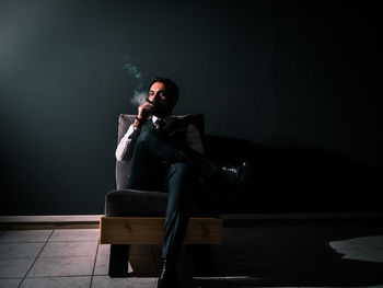 Man smoking cigar while sitting on chair at night