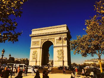 Low angle view of tourists against clear blue sky