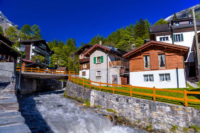 Houses by canal against clear blue sky in city