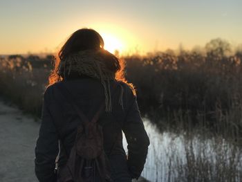 Rear view of woman standing against sky during sunset