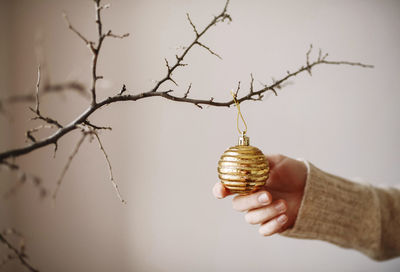 Cropped hand of woman touching bauble hanging on twig against wall during christmas