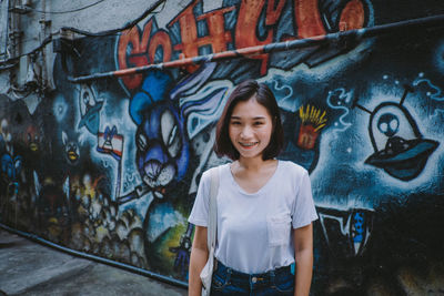 Portrait of smiling young woman standing against graffiti wall