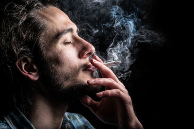 Close-up of young man smoking over black background