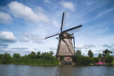 Traditional windmill by canal against sky