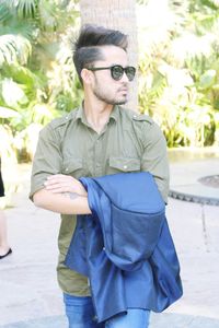 Young man wearing sunglasses standing against tree