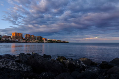 Sea by buildings against sky during sunset