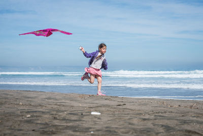 Full length of girl with kite running at beach against sky