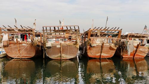 Fishing boats moored at harbor against sky