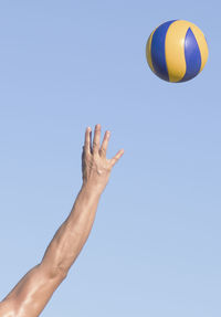 Low angle view of hand playing against clear blue sky with ball