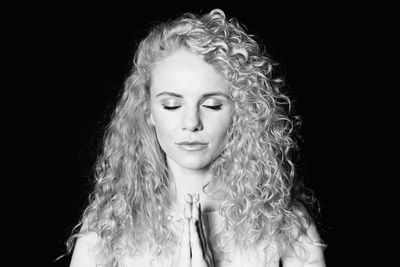 Woman with curly hair praying against black background