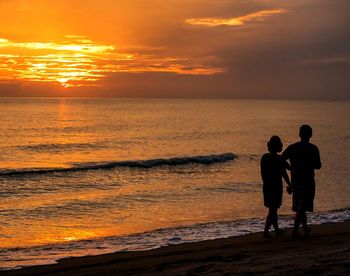 Silhouette friends standing at beach during sunset