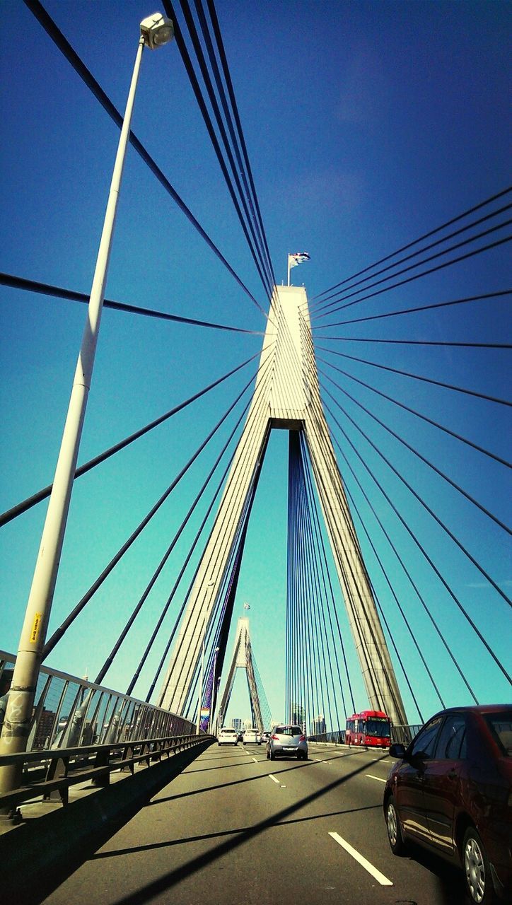 transportation, connection, bridge - man made structure, engineering, blue, the way forward, built structure, clear sky, suspension bridge, road, architecture, car, bridge, mode of transport, diminishing perspective, land vehicle, low angle view, sky, cable-stayed bridge, vanishing point