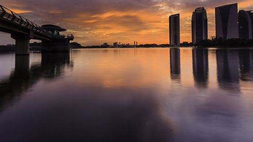 Bridge over river by buildings against sky during sunset