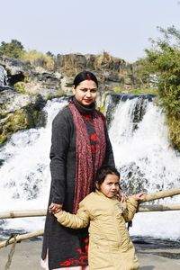 Portrait of smiling woman and her daughter standing against waterfall