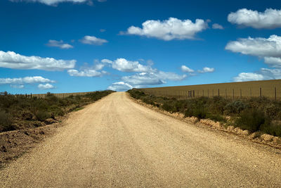 Dirt road amidst land against sky