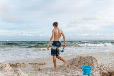 Rear view of shirtless man on beach against sky