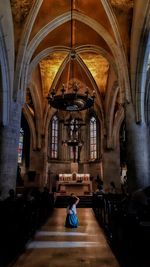 Rear view of woman photographing while kneeling in church