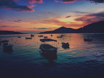 Sailboats moored in sea against sky during sunset