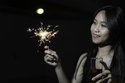 Young woman holding sparkler at night