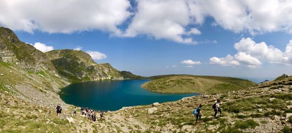 High angle view of people standing on mountain by lake against blue sky