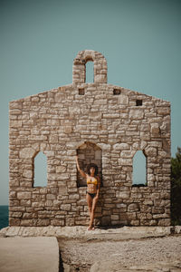 Woman wearing bikini standing against stone wall