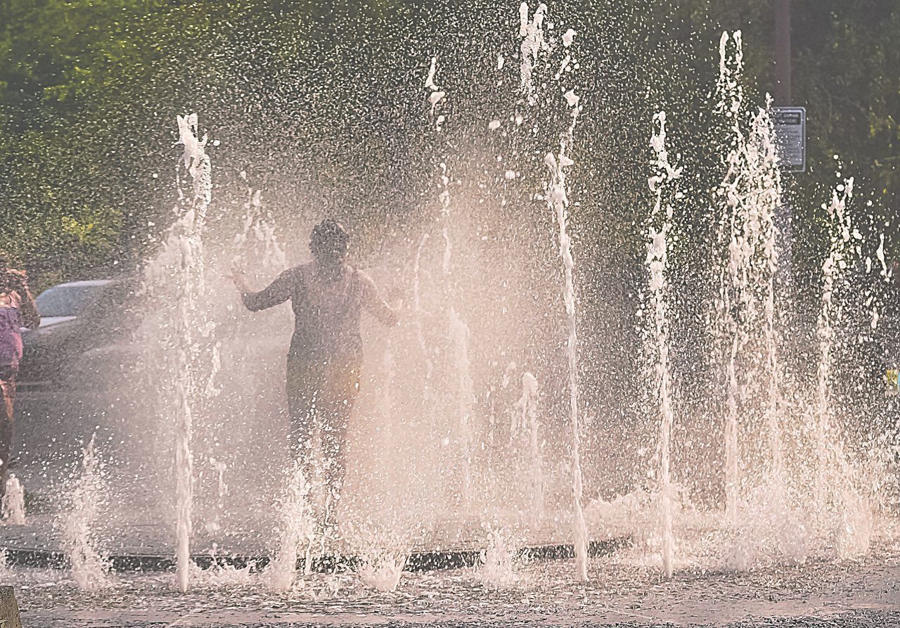 SILHOUETTE OF MAN SPLASHING WATER FOUNTAIN IN PARK