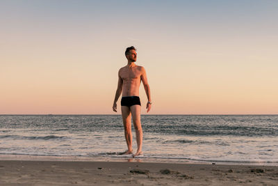 Young man standing on beach against clear sky