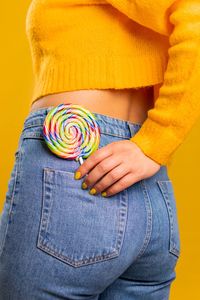 Midsection of woman with lollipop in pocket against yellow background