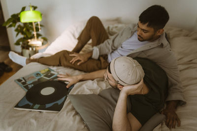 Gay couple with vinyl record talking to each other while lying on bed at home