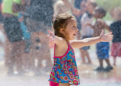 Little girl welcomes summer with open arms as she plays in a splash pad
