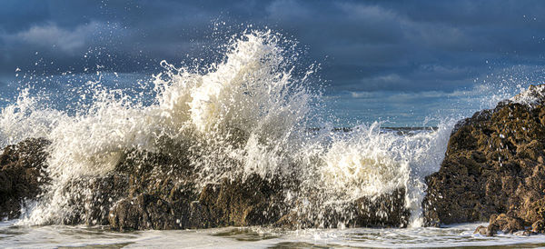 Sea waves splashing on rocks against sky