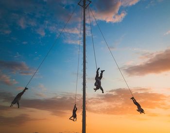 Low angle view of silhouette man hanging on rope against sky