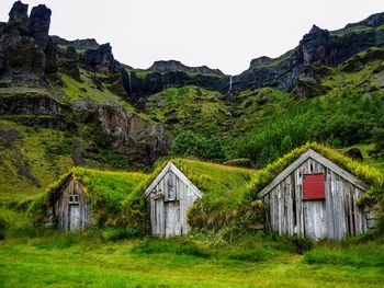 Plants covered old log cabins against mountains