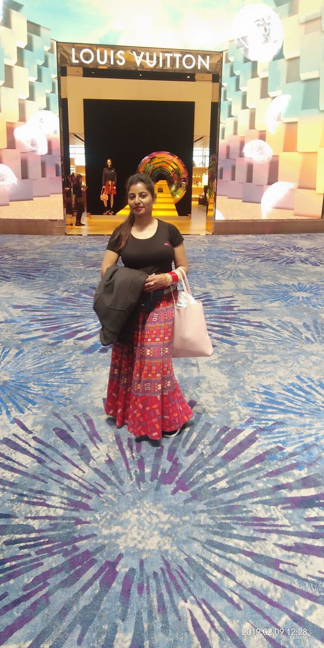 WOMAN LOOKING AT CAMERA WHILE STANDING AGAINST ILLUMINATED TRADITIONAL CLOTHING