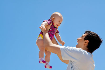 Low angle view of father playing with baby against clear blue sky