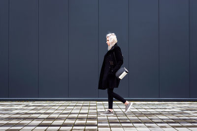 Side view of woman standing on footpath against wall