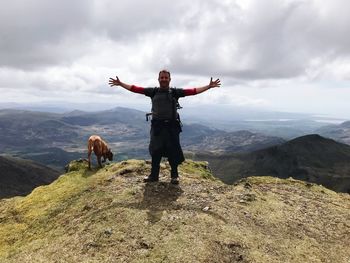 Man with arms outstretched standing on mountain against sky