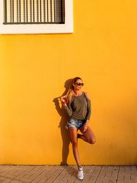 Full length portrait of woman standing against yellow wall