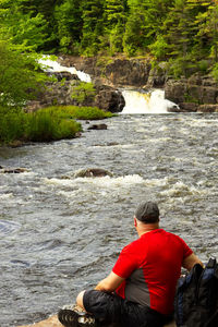 Rear view of man sitting on rock by river
