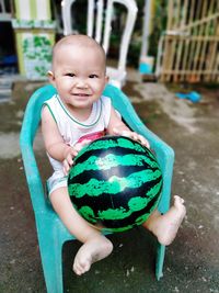 Portrait of cute boy holding ball sitting on chair outdoors