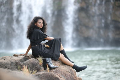 Portrait of woman sitting on rock against waterfall