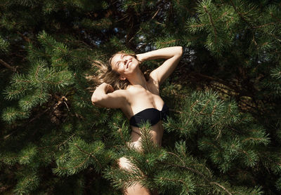 Full length of shirtless young woman standing against trees