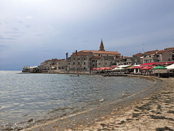 View of buildings by sea against sky in city